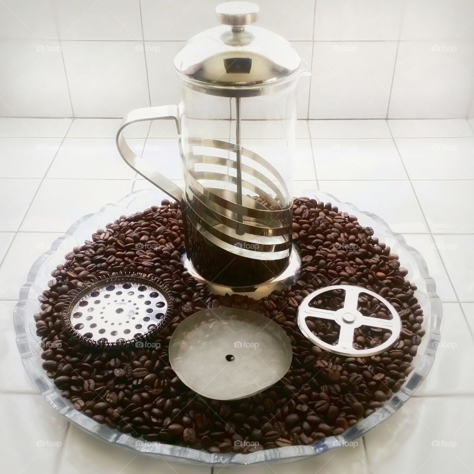 French press coffee maker on a bed of whole coffee beans on a round tray with the strainer separated into circles