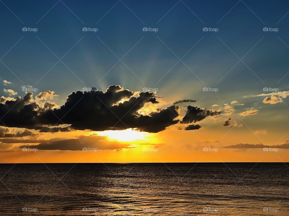 Light rays from the sunset form upward bursts through the clouds.