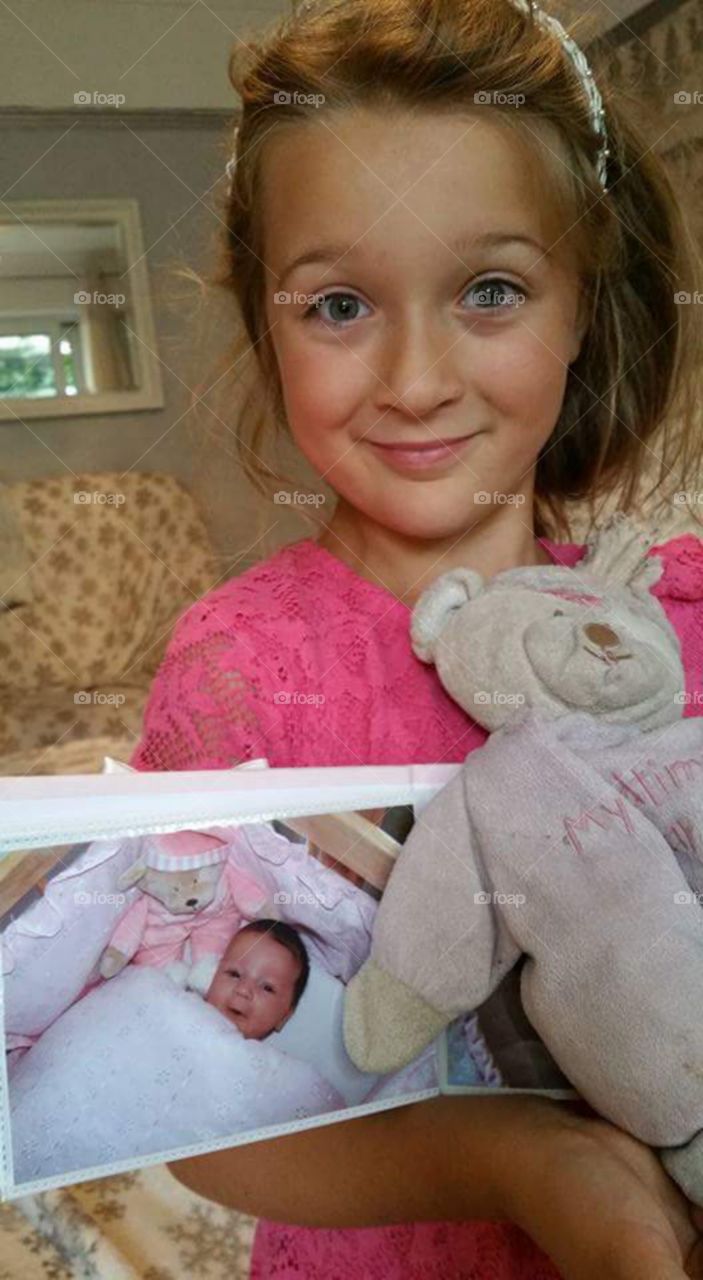 little girl showing an old photo of herself as a baby still with her favorite bedtime bear teddy toy