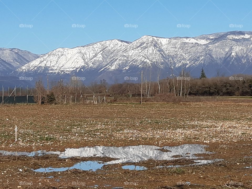 reflection of the mountains covered by snow in the puddle
