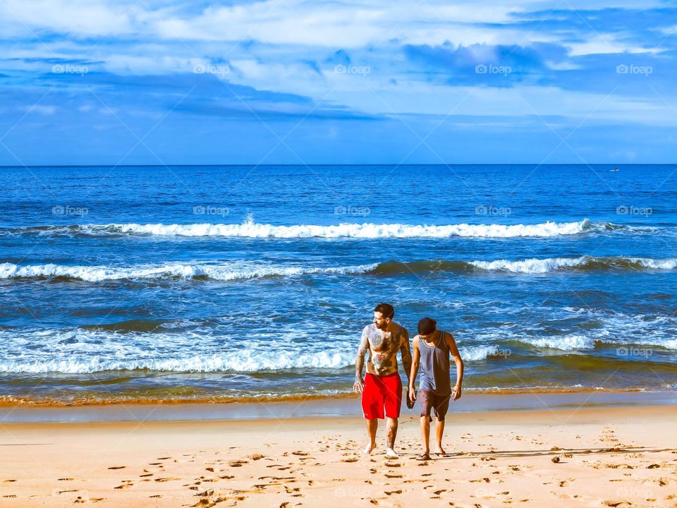 Beautiful shot of the Sunrise on the Atlantic ocean, in Praia do Sono, Brasil. There are 2 men on the beach sand, with a beautiful blue sky ahead.