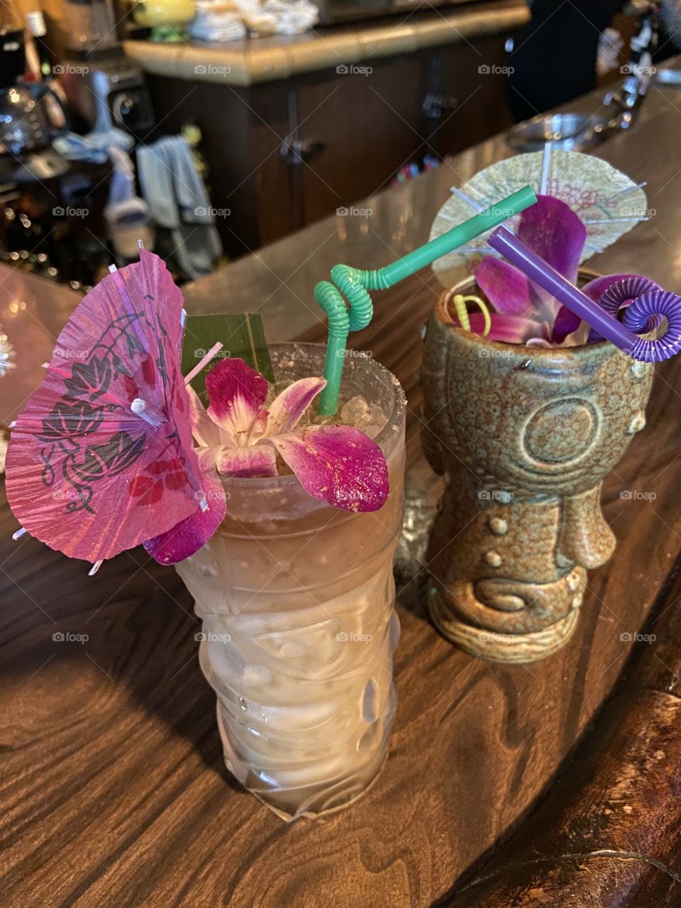 Bright beautiful strong tiki drinks in exotic mugs with umbrella and flower garnishes. 