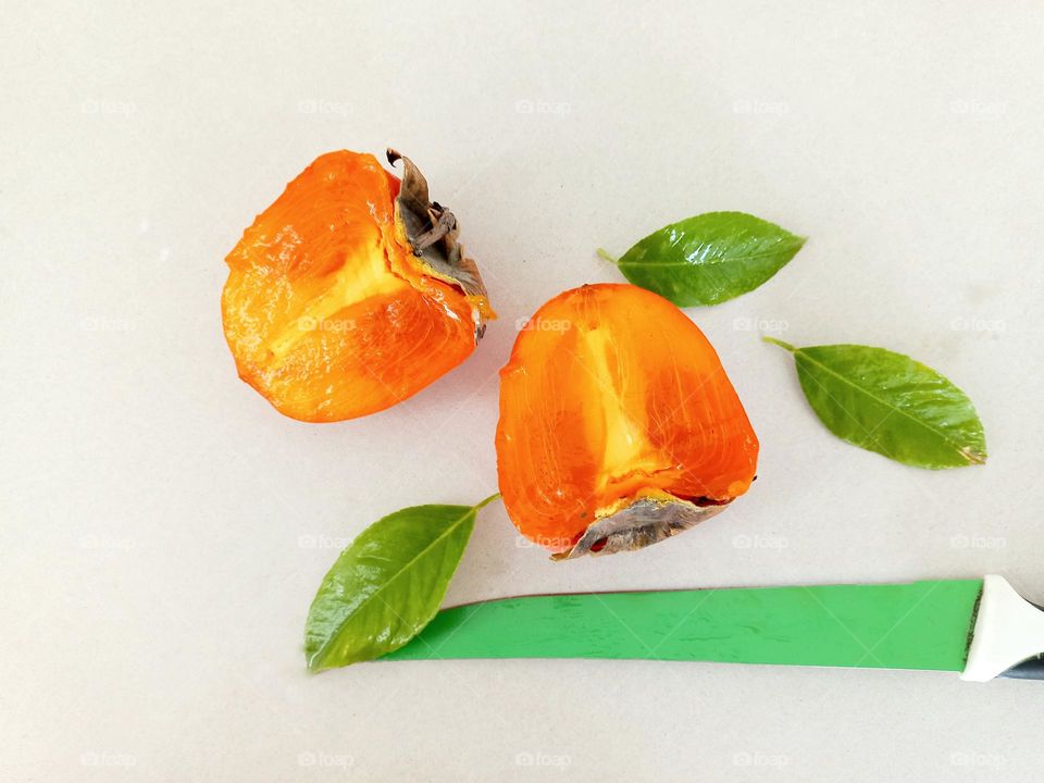 orange persimmon slices and a green knife.