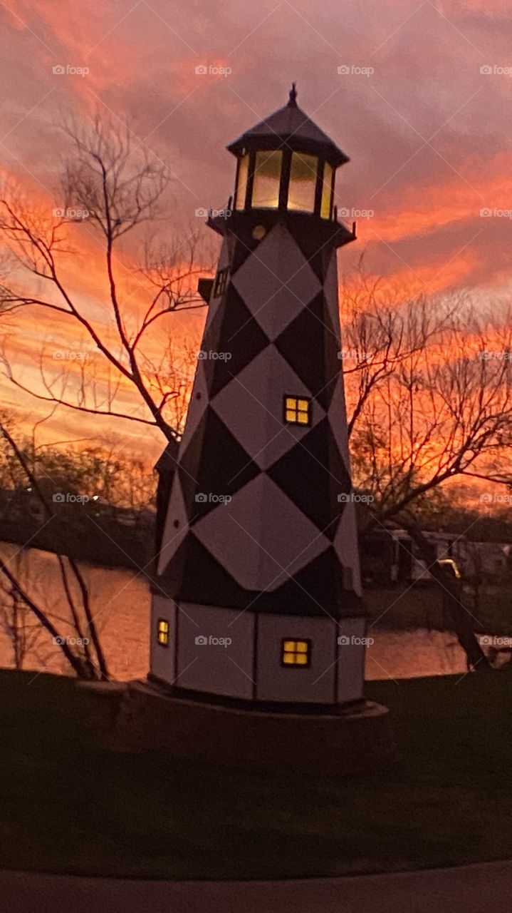 Sundown Completed Sky is opening up. Blistering Orange Slivers along with Yellows upper atmosphere bleeding down to the lower with Grays Blues Violets tops of high clouds getting into the act by opening up. Lighthouse standing firm.