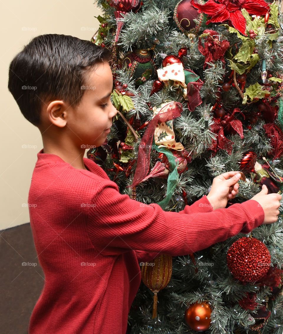 Decorating the Christmas Tree, young boy putting ornaments on the tree