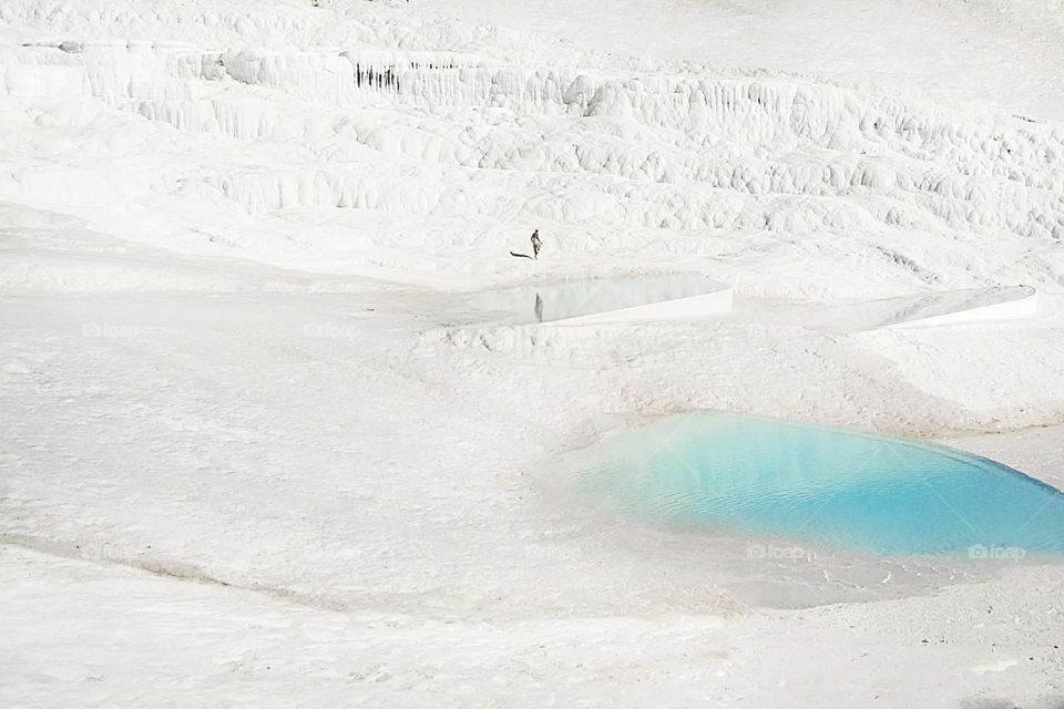 Tiny human walking by the white chalk mountain with blue water lagoons