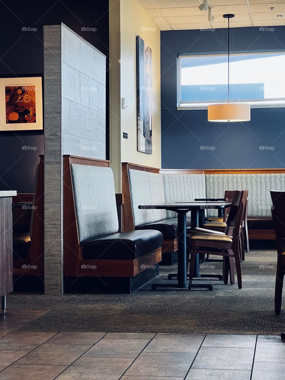 Simple lines and wooden furniture of cafe interior. Drop lighting and natural light from high window, carpet and padded benches.
