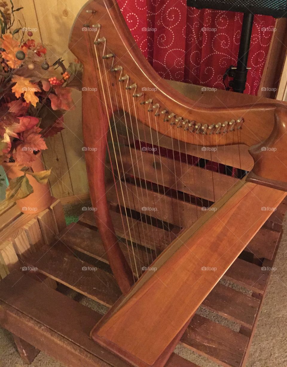 Wooden musical harp displayed on rustic chair with flowers beside the musical piece.