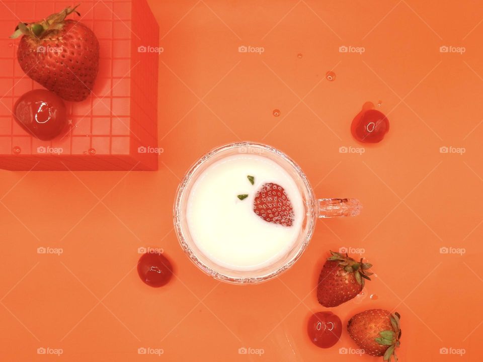 Fall color chosen in red with red background and block with strawberries and cherries with a strawberry that is floating in the milk in the small glass cup.