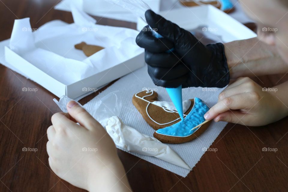 Work shop for glazing cookies. Hands doing glazing of yacht shaped cookie 