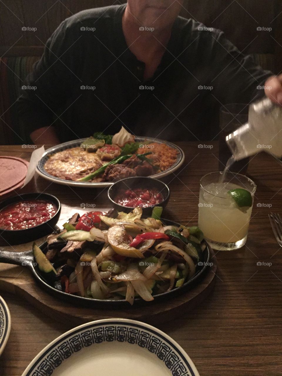 Restaurant table for two for warm romantic dinner featuring Mexican fajitas, chips, salsa, rice, refried beans, cheese, lime, salt, margarita, cilantro 