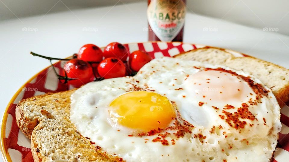 Breakfast of toast, runny eggs, and blistered tomatoes on the vine with Tabasco hot sauce