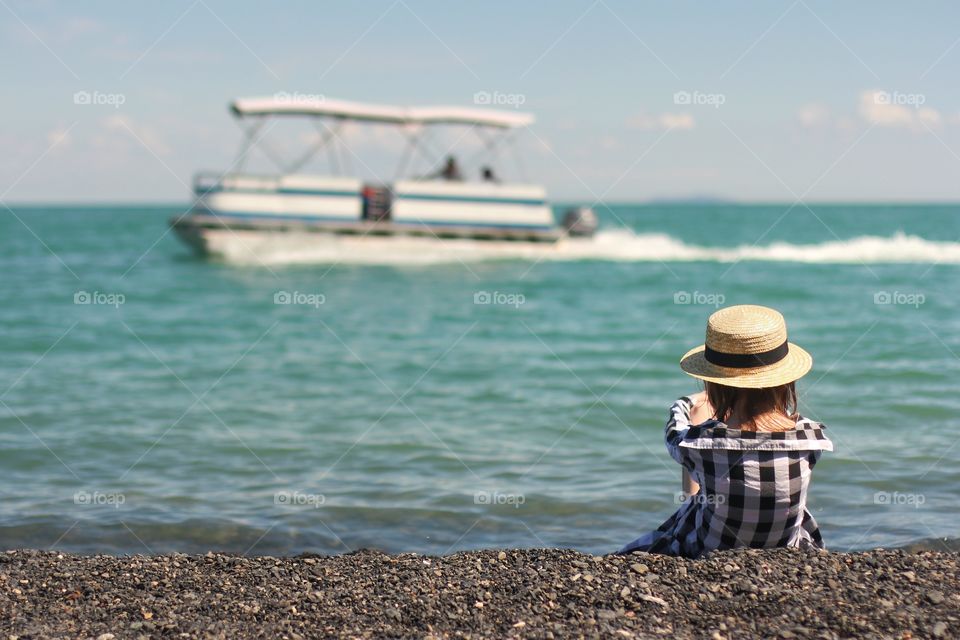 Little girl sits on the shore and looks at a pleasure boat