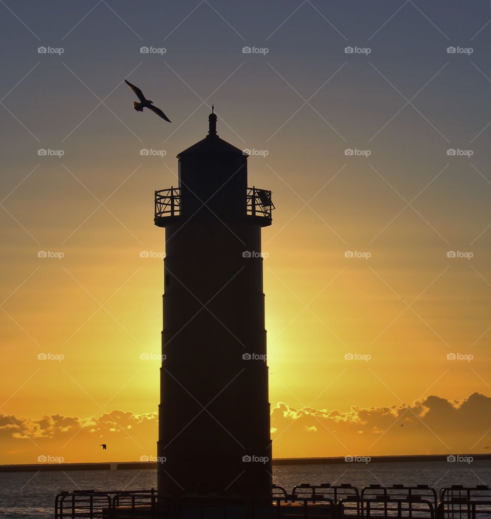 Silhouette of light house near the sea at sunset