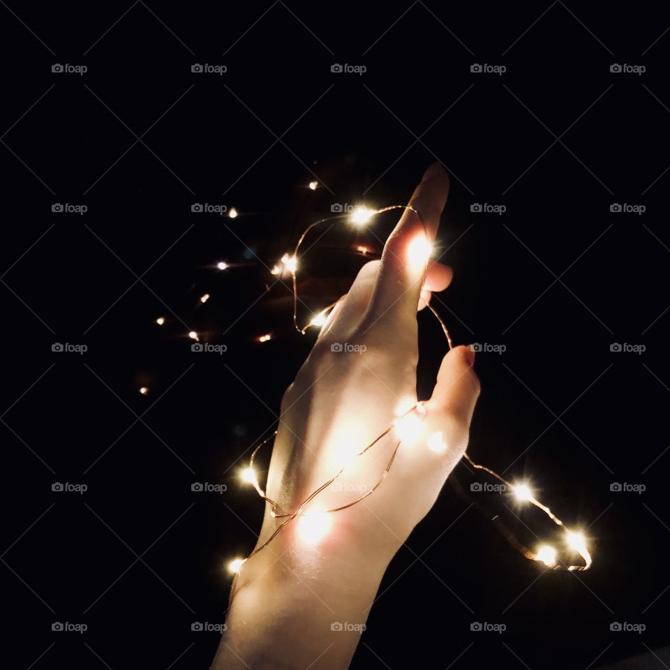 A hand playing with beautiful fairy lights in the dark.