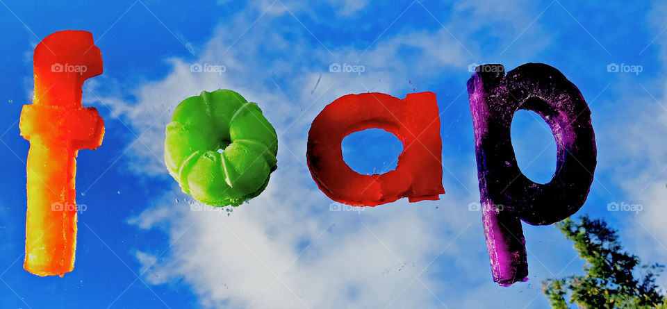 The foap name spelled out in jello letters and placed on a mirror outside on a sunny, partially cloudy, day. There is a reflection of the clouds and a tip of a tree and the letters look like they’re floating in the sky!