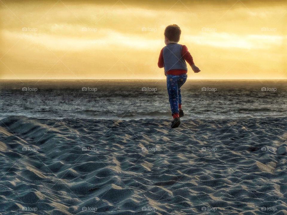 Boy Running Across Sand Toward Sunset
