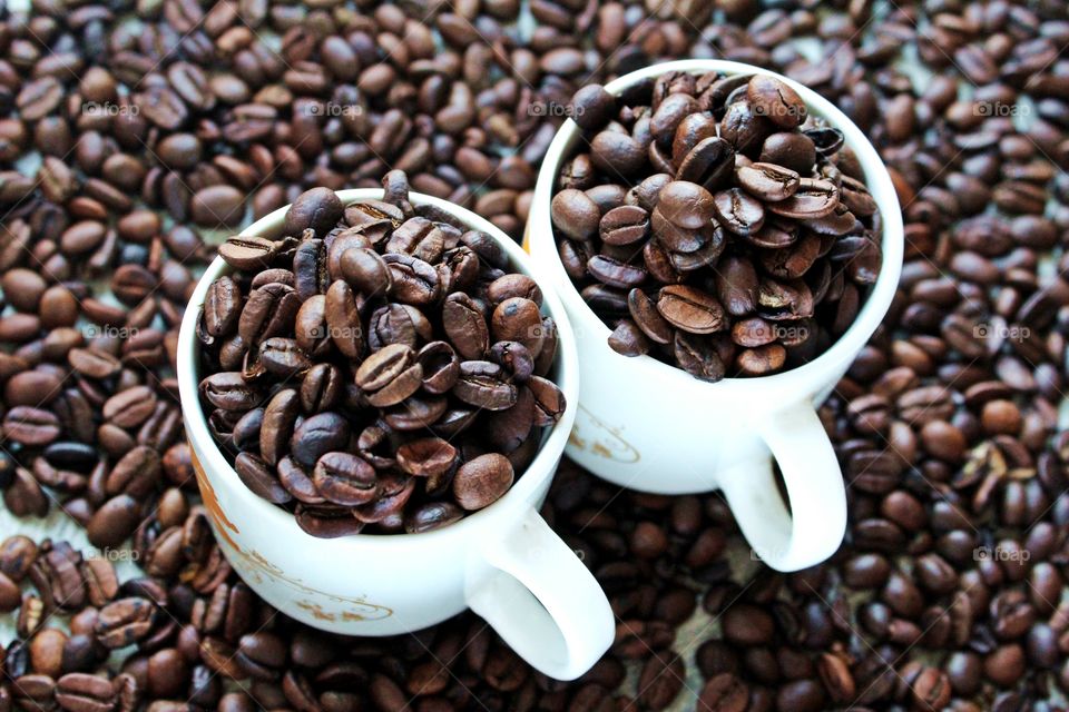 Two cups of coffee beans on coffee beans background.