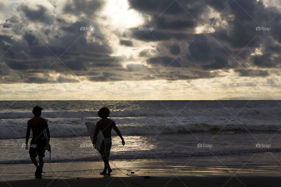 Silhouette of two boys walking at beach with surfboard