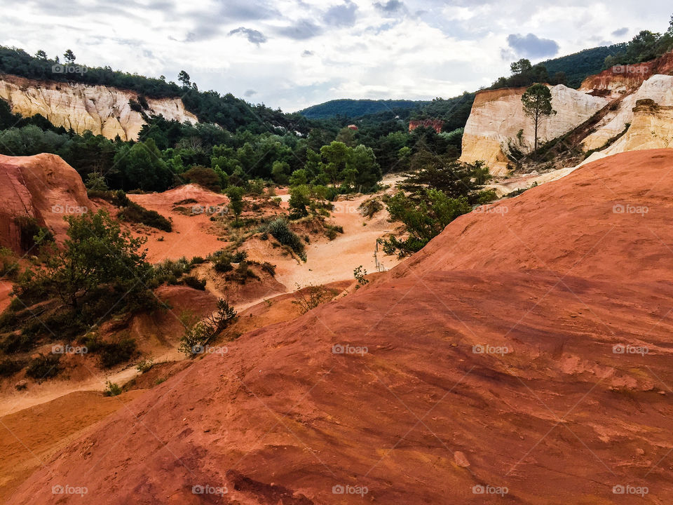 Nature reserve called Colorado Provencal in France with trees and orange colored sand duned high as mountains a rainy day in summer.