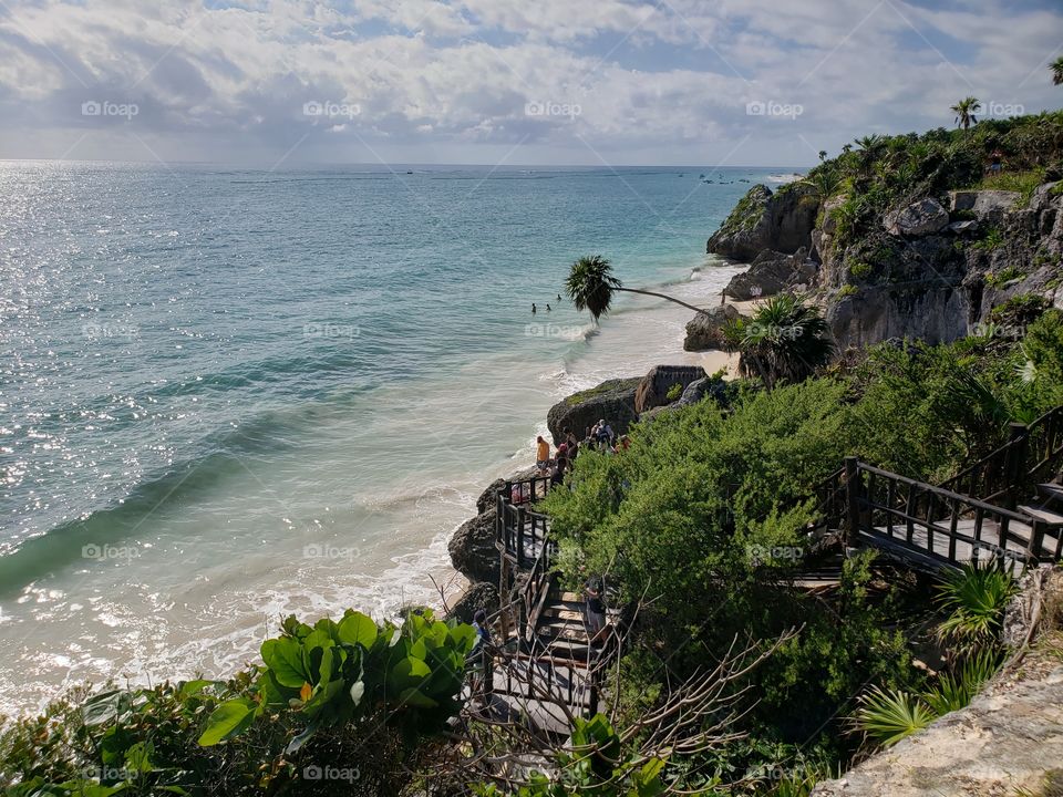 View from above, stunning beach with lush green cliffs, palm trees, blue ocean, and cloudy skies in Mexico.