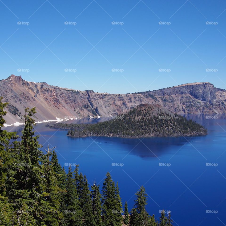 The jagged rim reflecting into the rich blue waters of Crater Lake in Southern Oregon on a beautiful summer morning with perfect clear blue skies. 