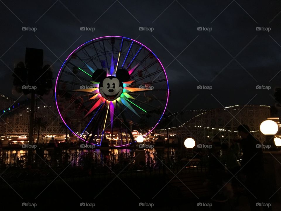 A colorful, night time view of Disney Land’s pier and ferris wheel. 