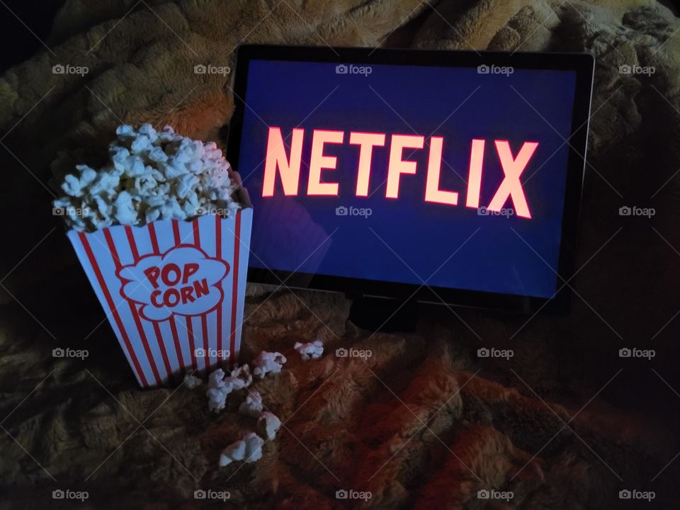 Laptop computer screen ready to watch Netflix for a fun, cozy, and relaxing night with popcorn as a snack, on soft bed blanket in dark room