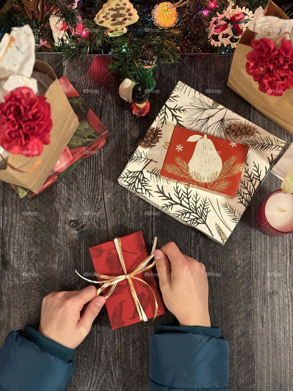 Man’s hands, wrapping red Christmas gift, tying a bow. Top down view, festive scene.