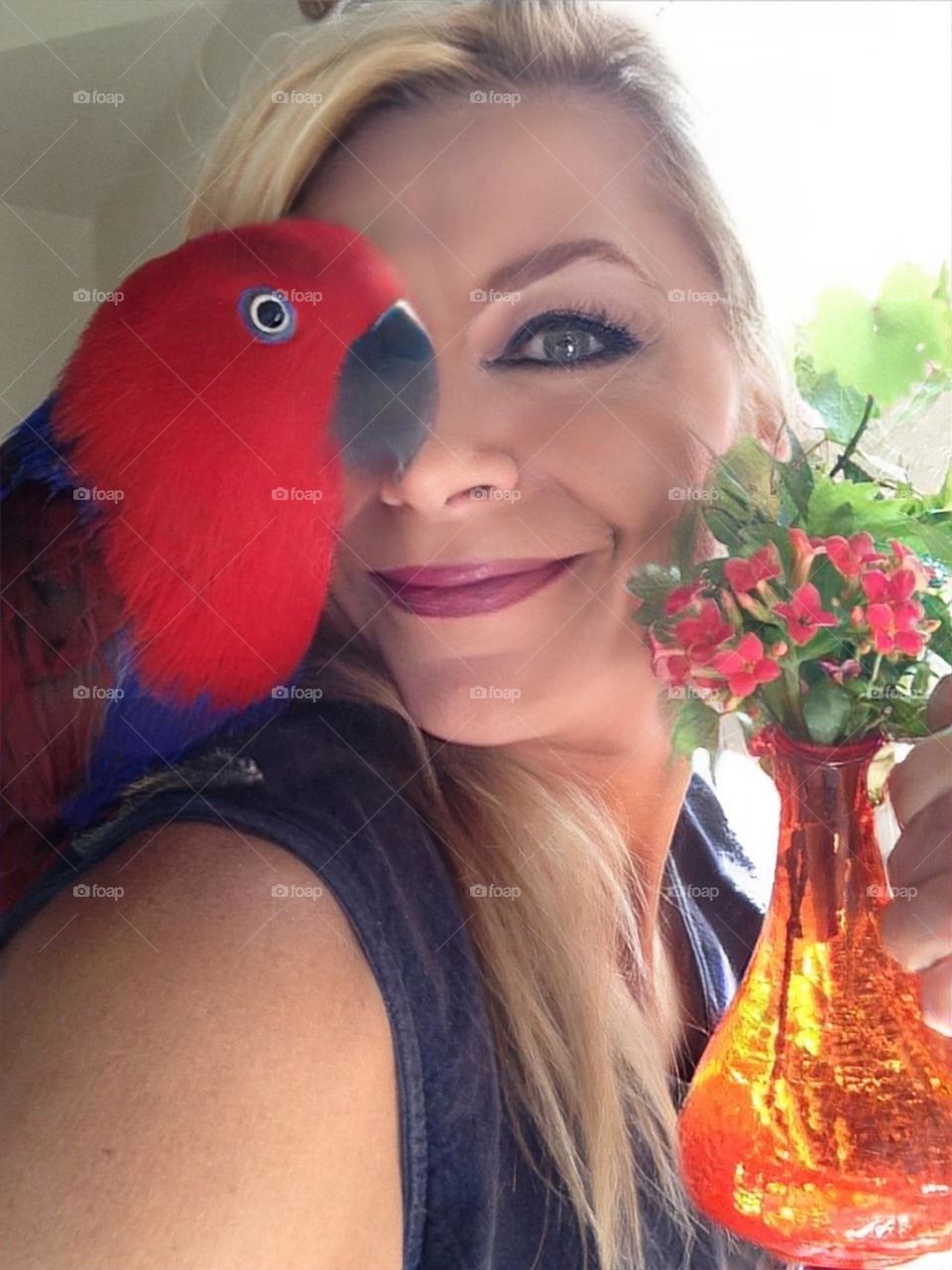 A lady a red parrot and flowers.