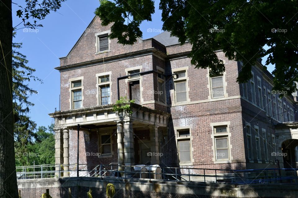 A historical abandoned brick building with a railed walkway in front and overgrown plants