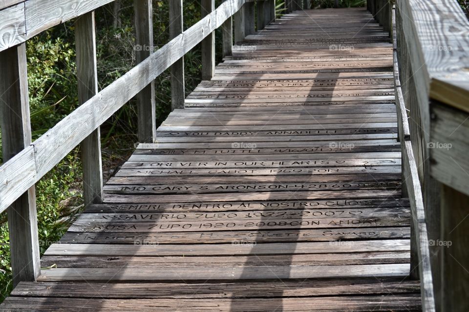 A wooden plank boardwalk bridge with engraved words on the planks 