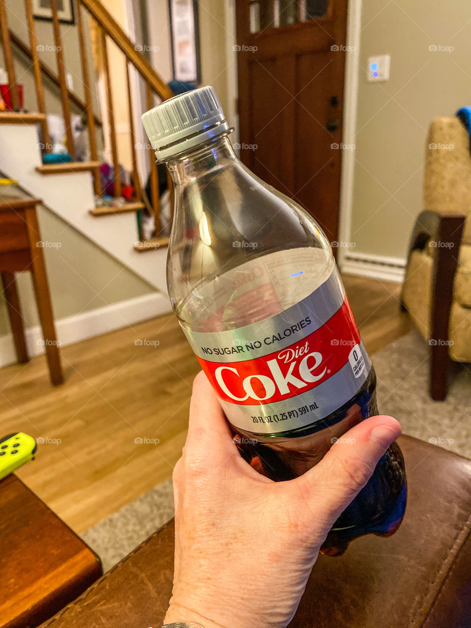 Have a a coke and a smile...bottle of Diet Coke being held by a woman while watching tv in her living room. Simple shot, hand in frame.