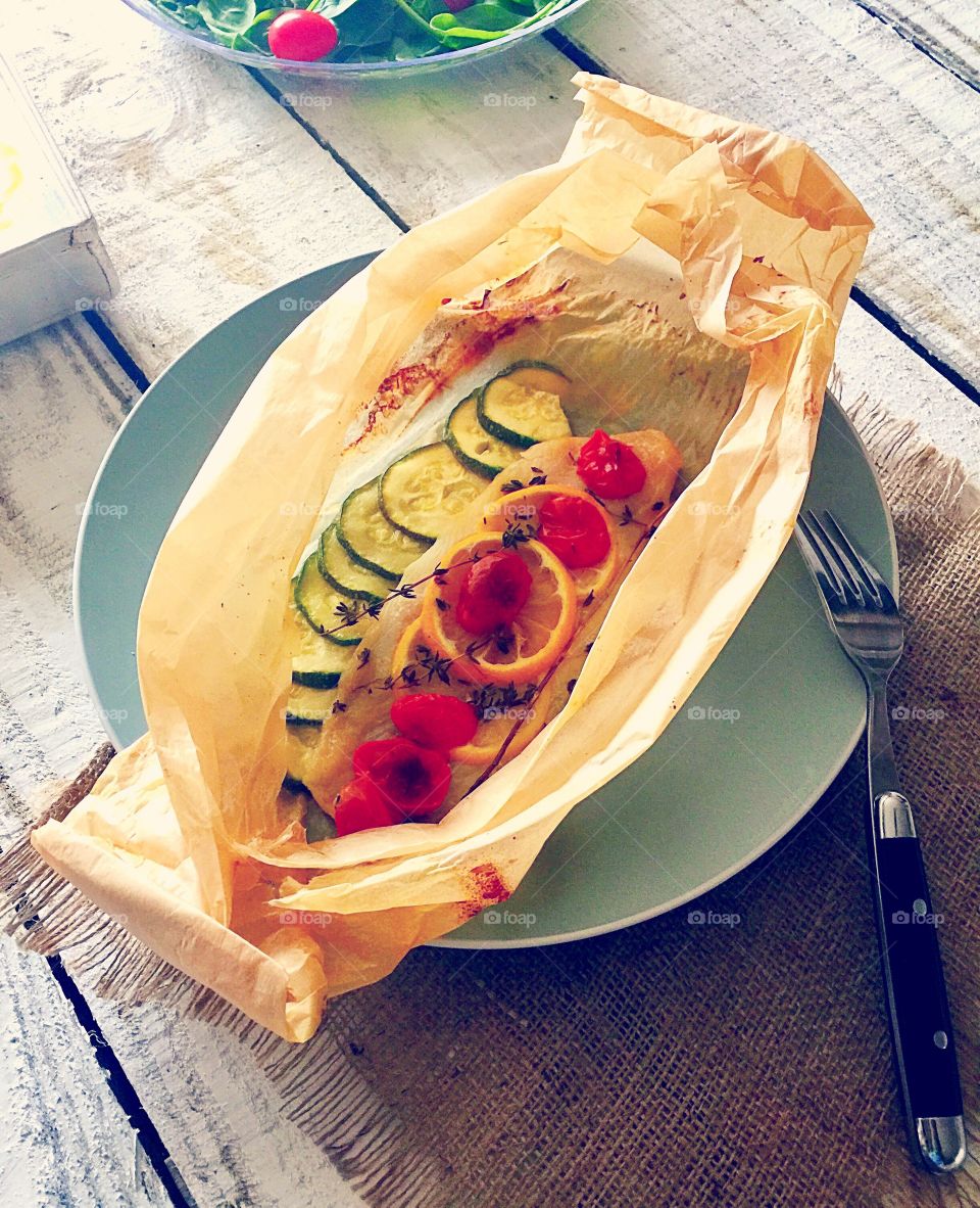 Fish baked with courgettes tomatoes and lemon and herbs in a papillote (in a paper bag)