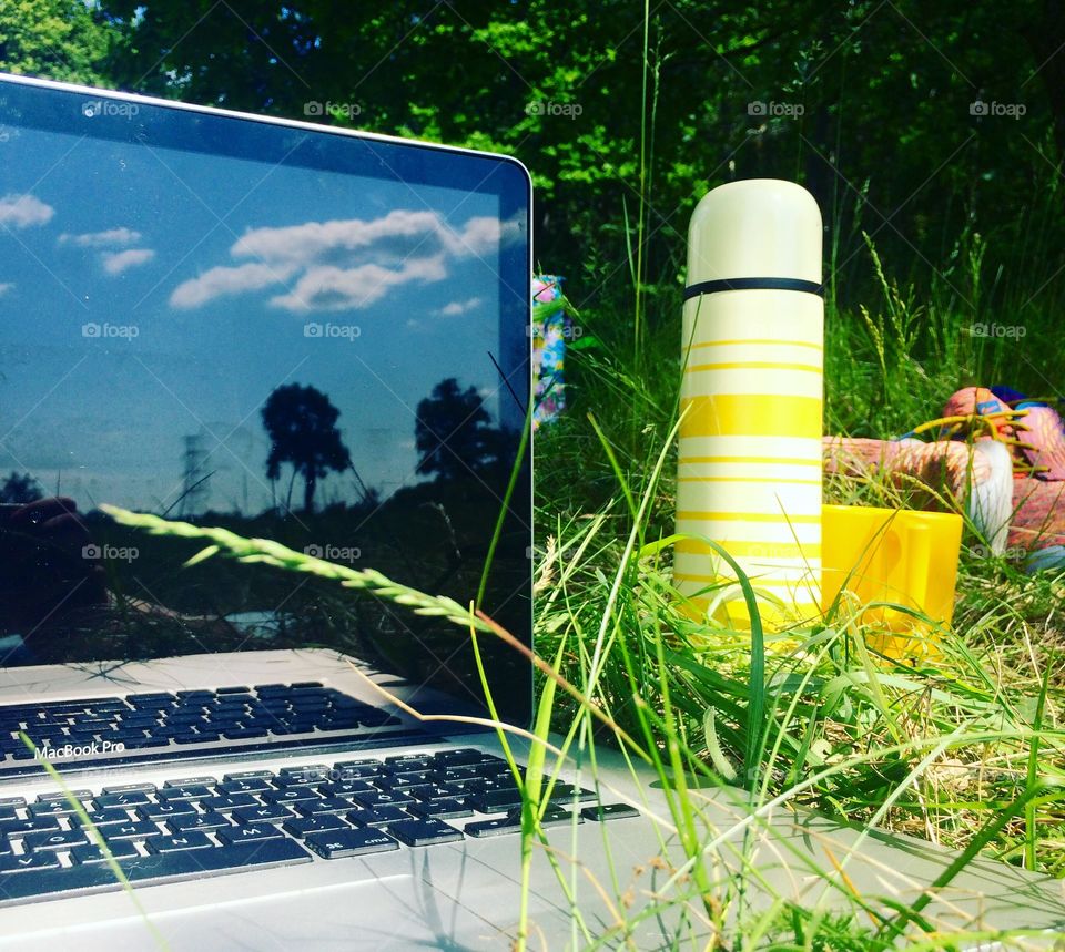 Computer and coffee mug in grass