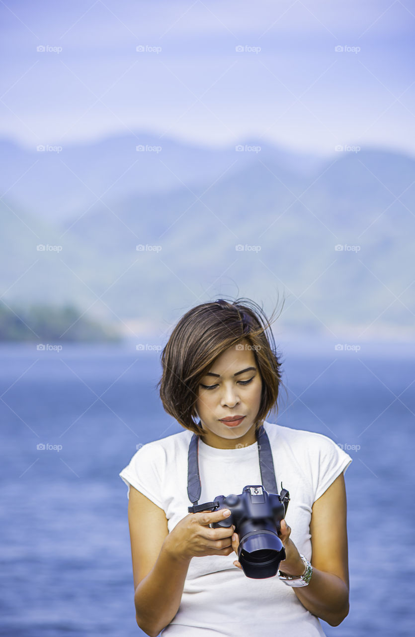 Hand woman holding the camera background Kaeng Krachan dam phetchaburi , Thailand.