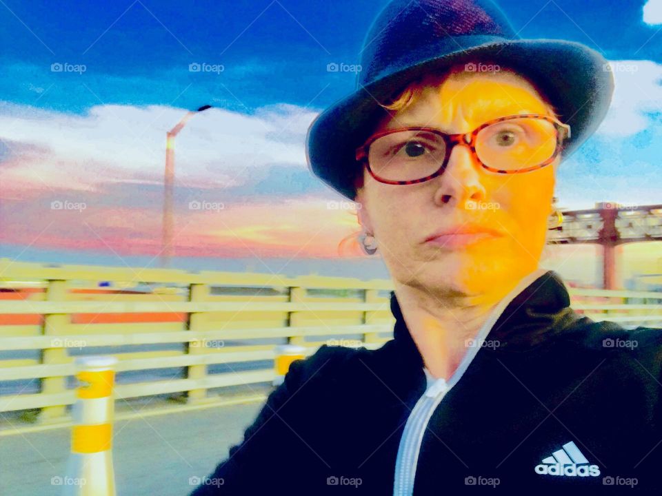 A closeup self portrait set against the railing sectioning off the car lanes on top of the Pulaski Bridge that leads from LIC, Queens to Greenpoint, Bklyn, NY photographed on a lovely Spring time afternoon in 2019. Hypnotic Productions