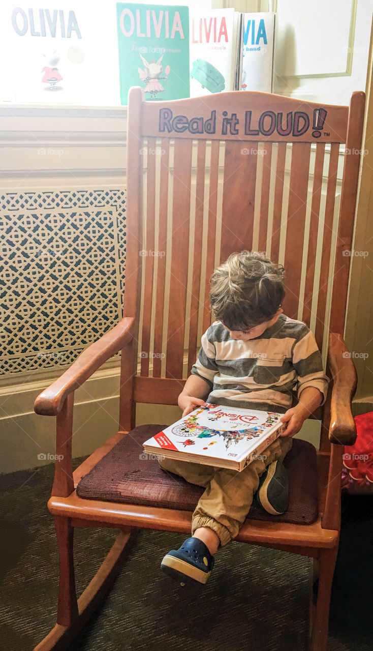 A child reads a book in a rocking chair in the Library of Congress children’s room. 