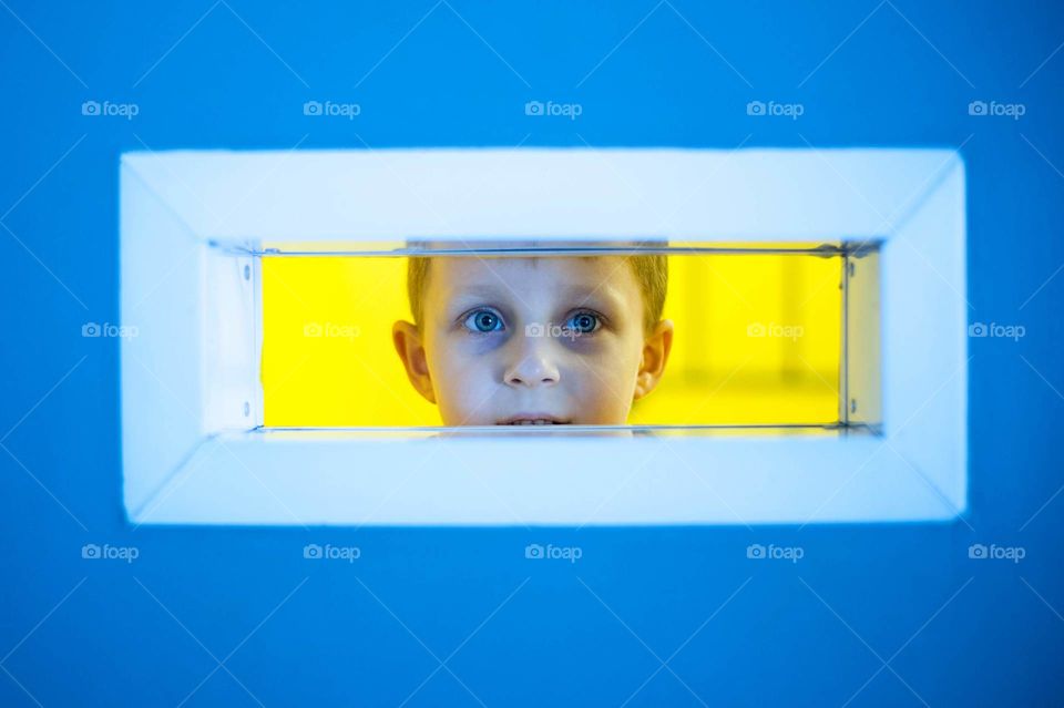 Small boy looks into out of the little window. Bright colours blue and yellow.