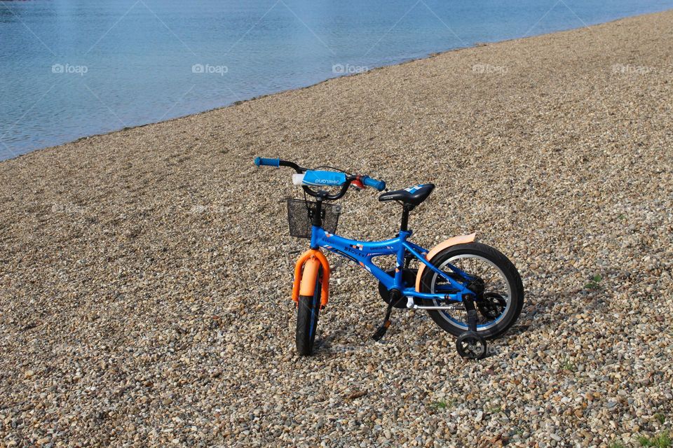 One blue-orange lonely children's bicycle on the shore by the lake