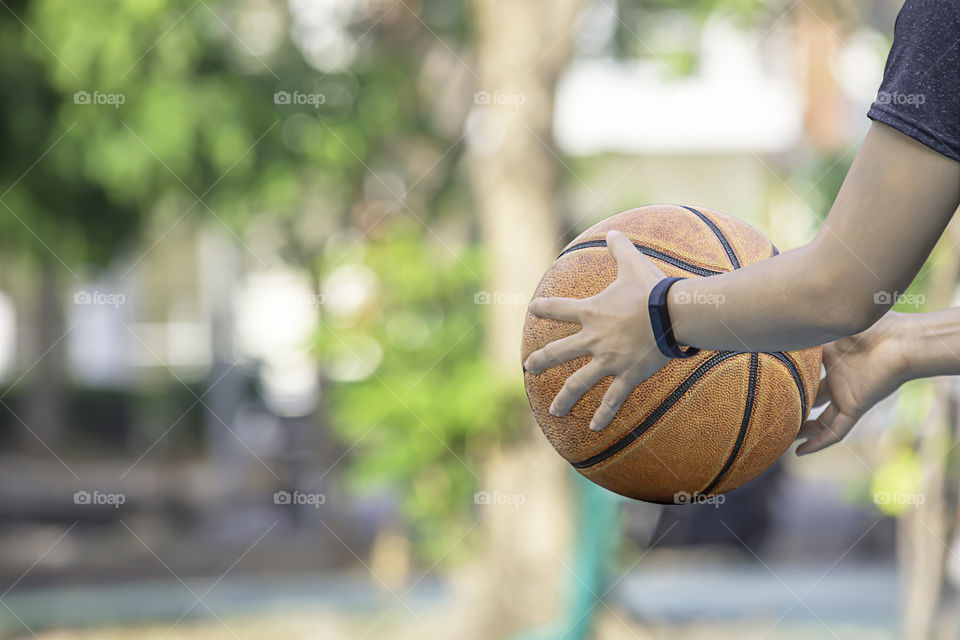 Leather basketball in hand of a woman wearing a watch Background blur tree in park.