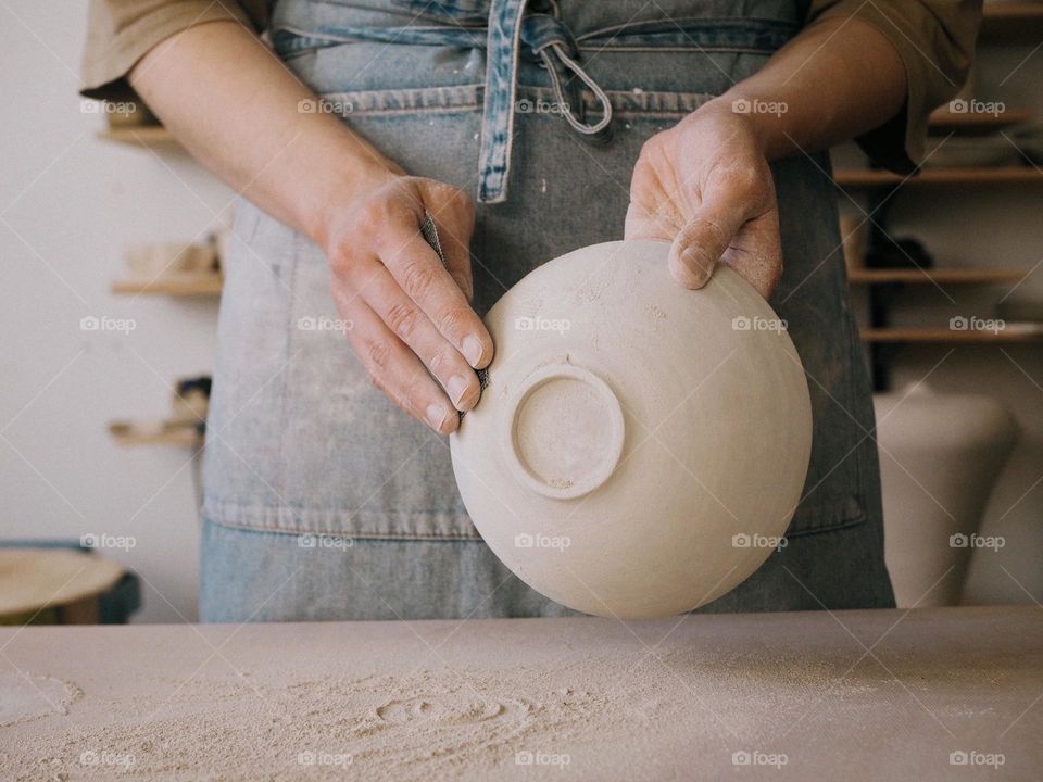 Unrecognizable woman ceramist peeling a clay plate holding sponge. The process of irregularities and grinding of the finished product. Small business, hobby, ceramic concept, circle 