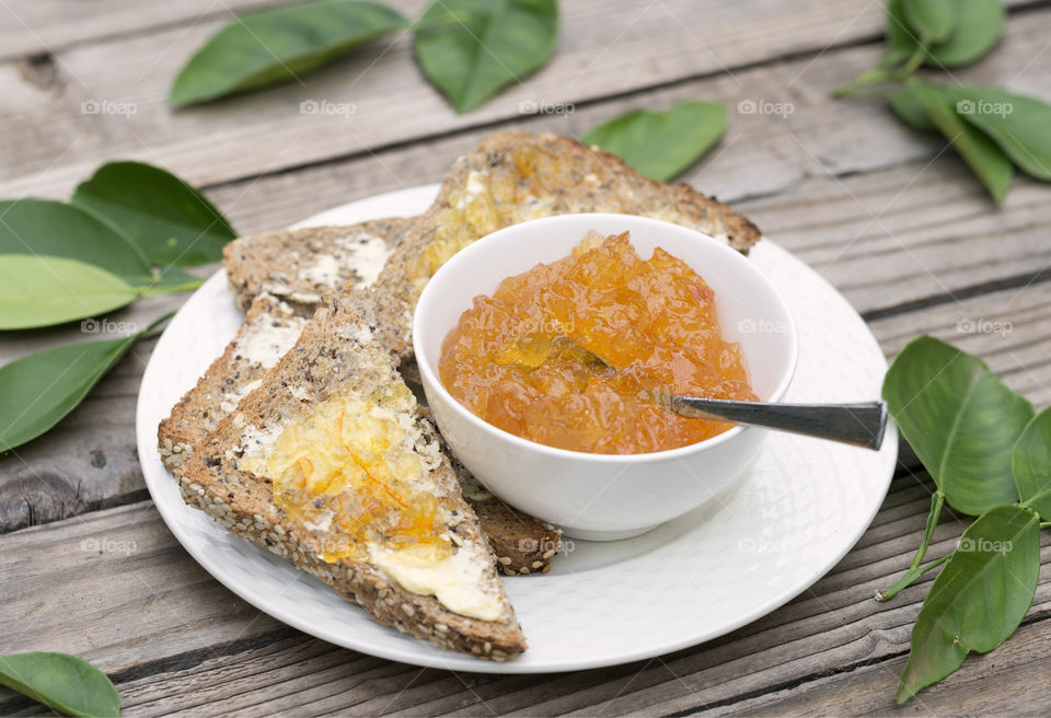 Toast spread with marmalade on a white plate with a white bowl filled wth homemade marmalade and a spoon.