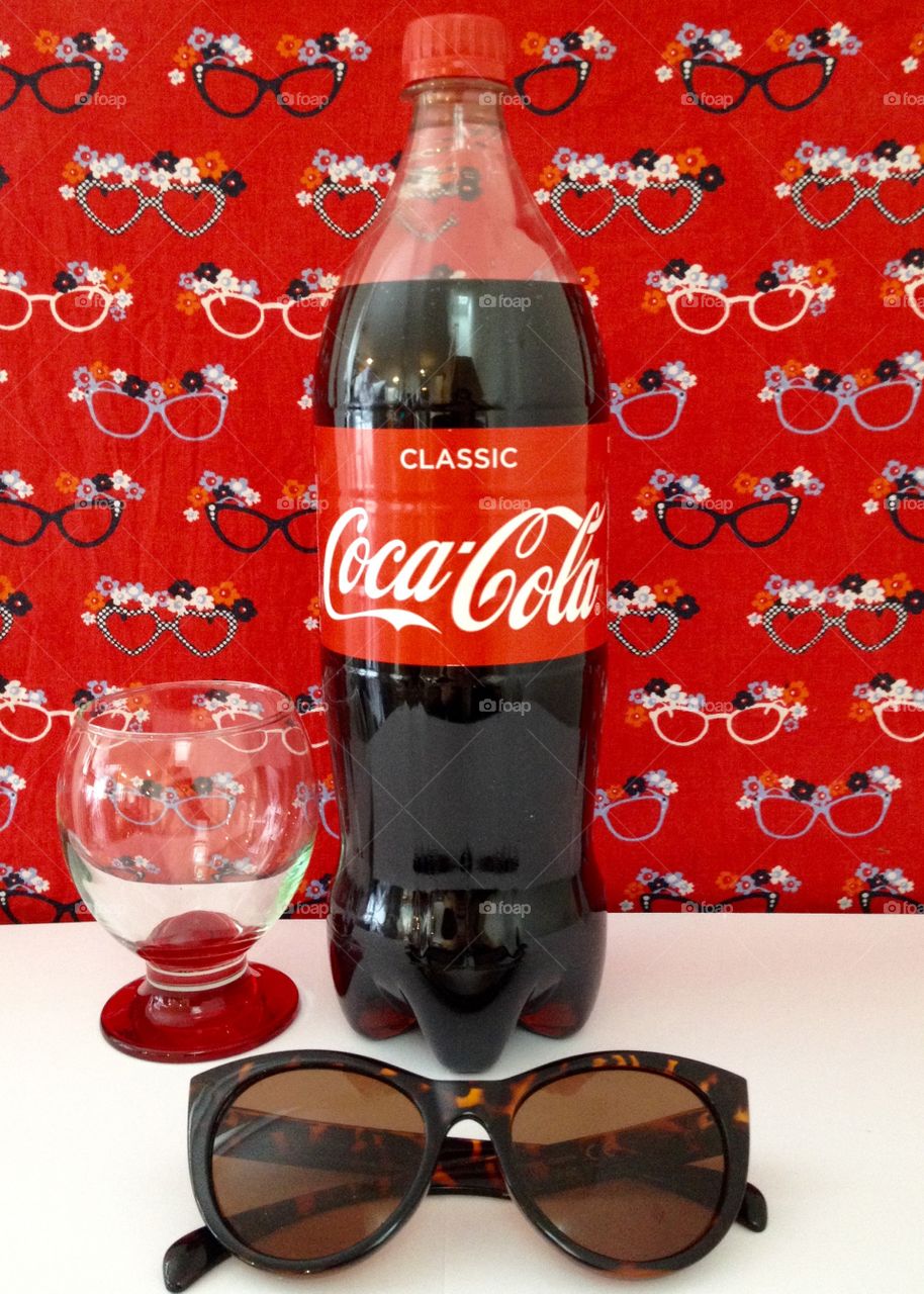 Coca Cola composition. Classic. Bottle, glass, sunglasses against red background 