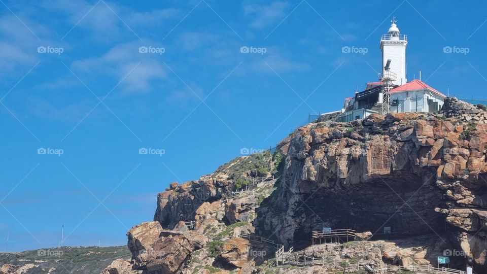 beautiful little lighthouse at the edge of a cliff.