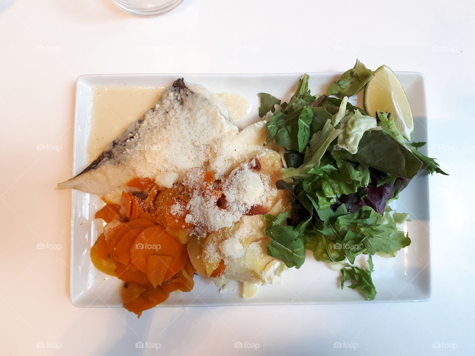 Plate with fish, salad, carrot, potato at the white table. Healthy dinner