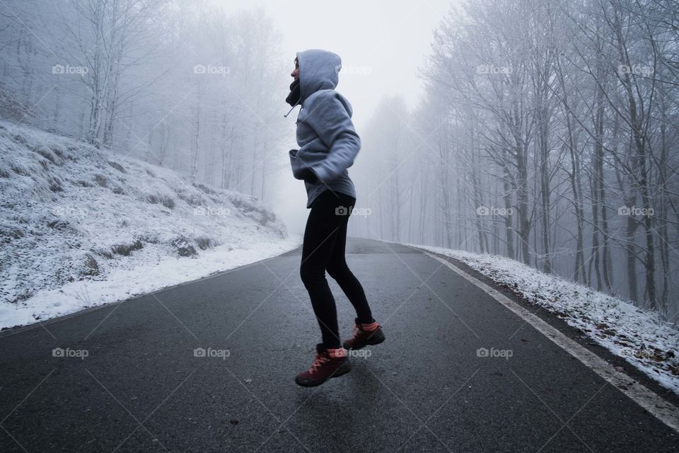 Girl jumping in the middle of a winter road.