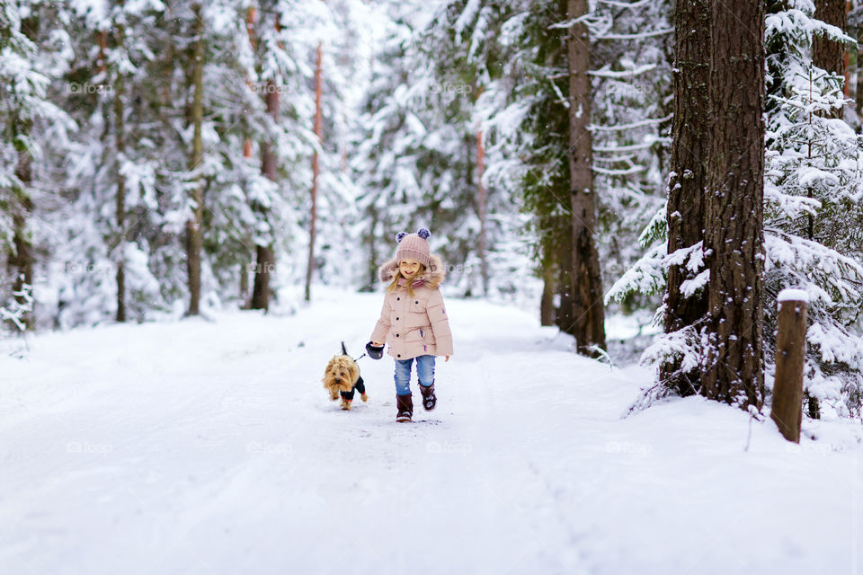 Cute little girl running on snowy forest with dog
