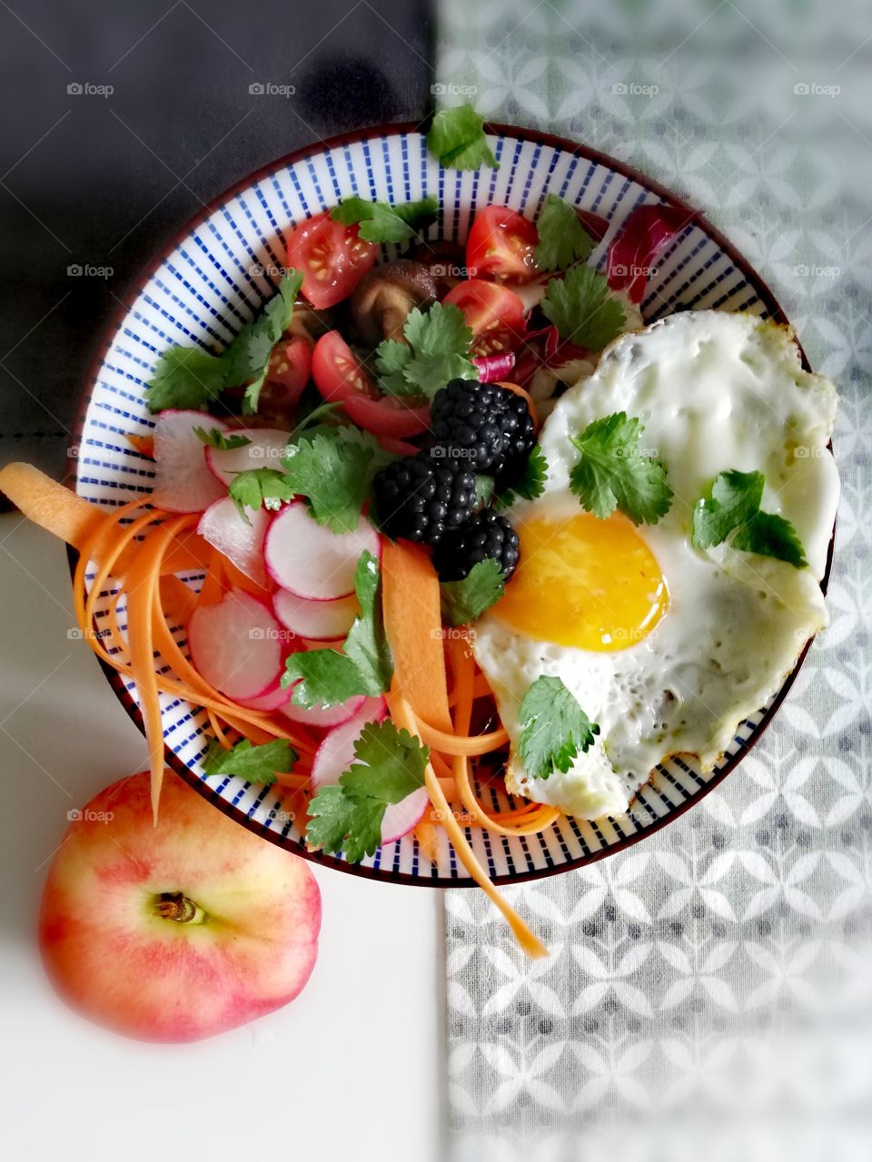 Bowl with fried egg, salad and berries, next to a peach