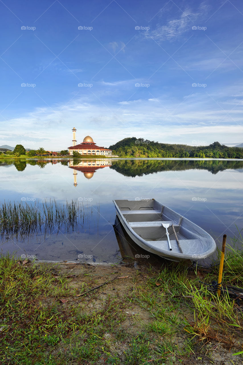 A boat and mosque reflections on the lake with blue sky background